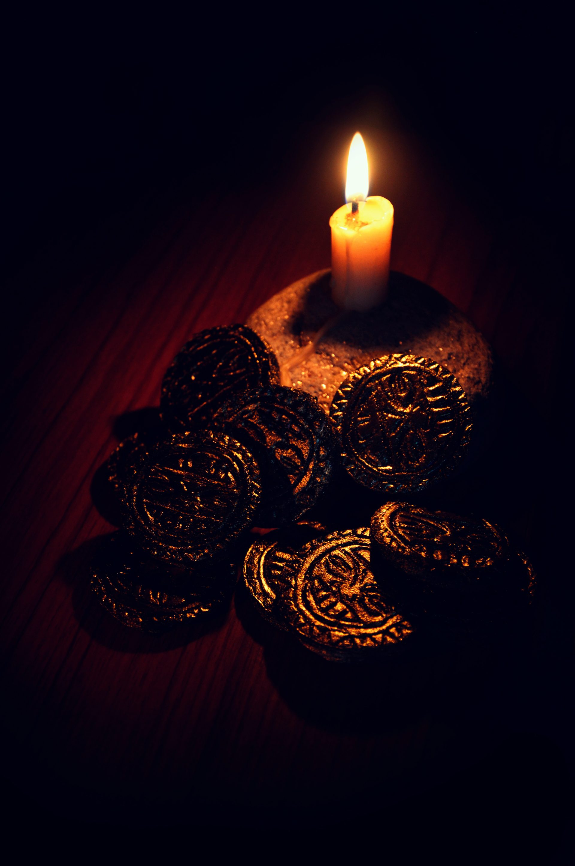 drei runde Goldmünzen neben einer weißen Kerze